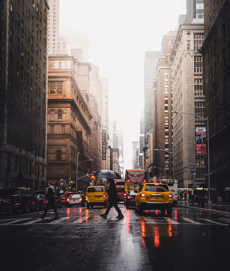 People crossing a wet city street with yellow taxis.